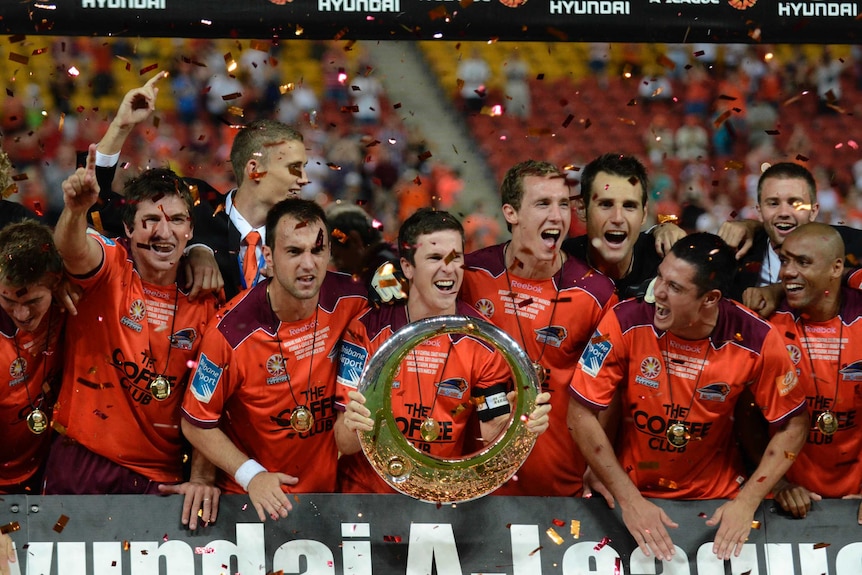 Matt McKay lifts the A-League trophy in front of his teammates