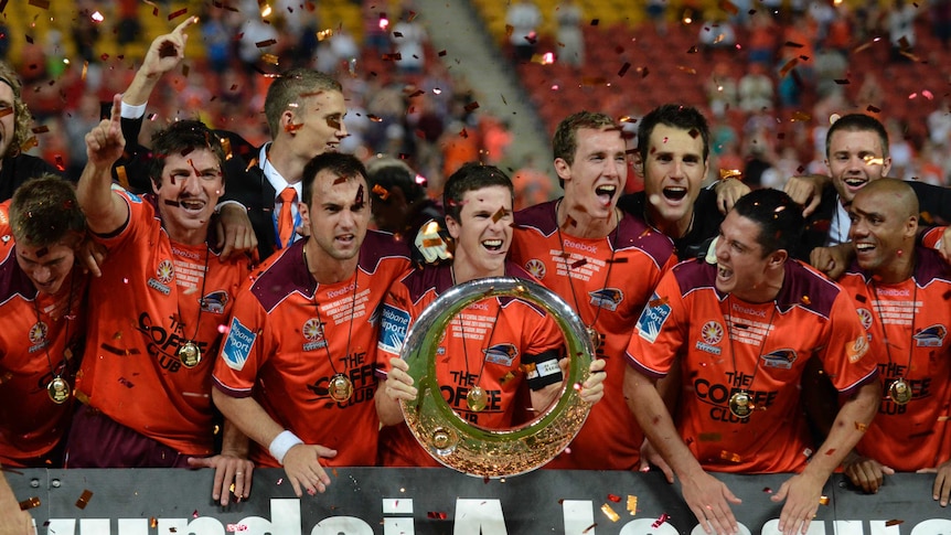 Matt McKay lifts the A-League trophy in front of his teammates