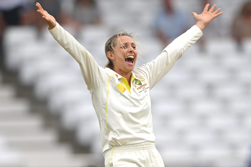 A cricketer has her arms above her head as she appeals for a wicket.