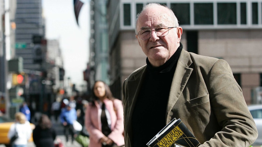 Clive James, wearing a corduroy jacket, holds his book of essays, Cultural Amnesia.