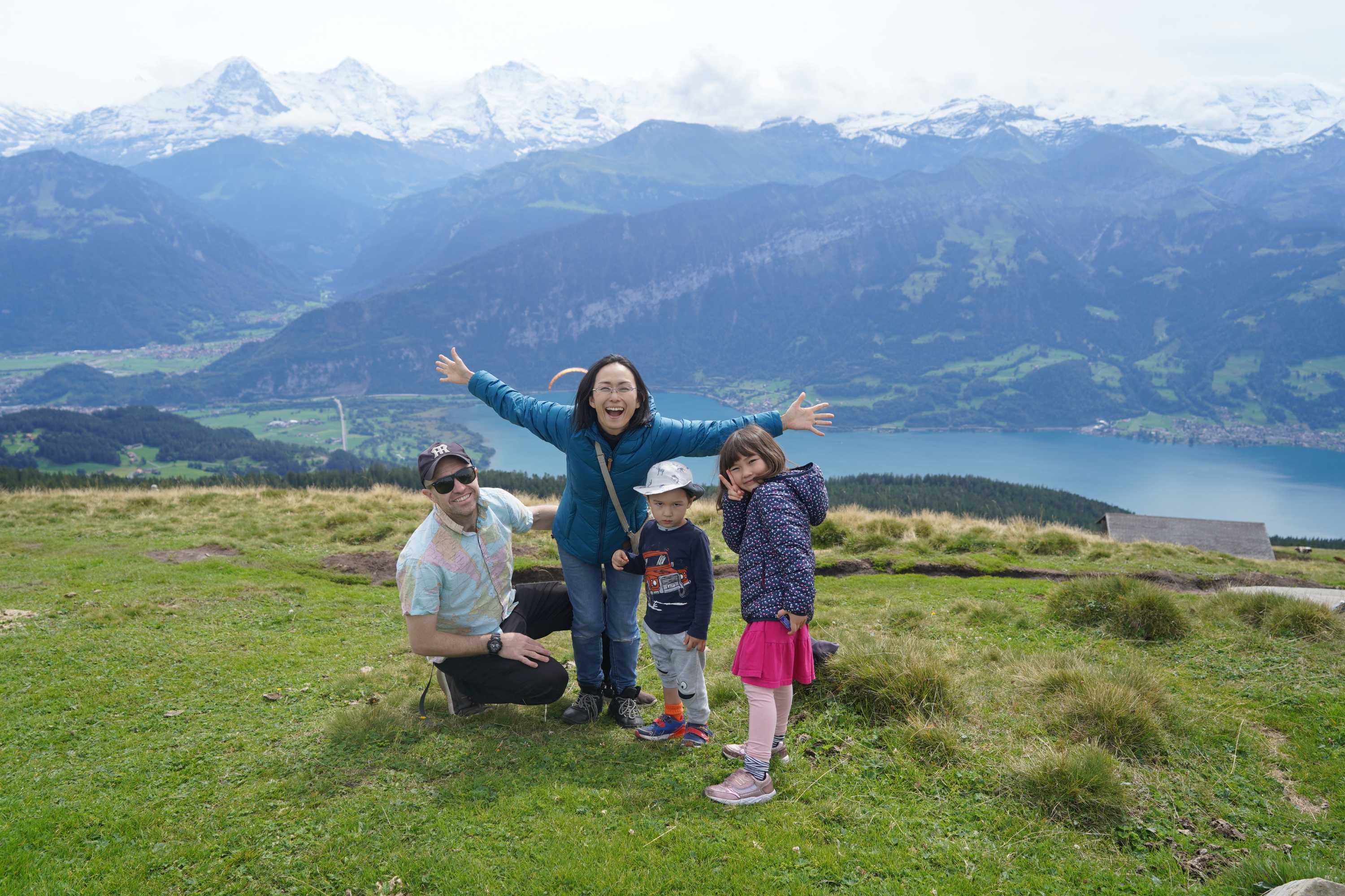 A family of four on a hill with mountains and a lake in the background.