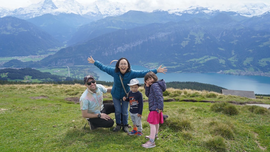 A family of four on a hill with mountains and a lake in the background.