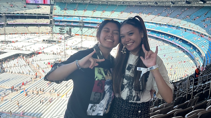 A portrait photo of two Filipino Australian women standing beside each other, smiling, in the stands of a large stadium