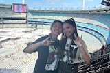 A portrait photo of two Filipino Australian women standing beside each other, smiling, in the stands of a large stadium