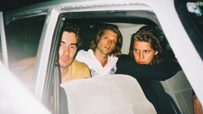 Mansionair band members sitting the back of a car, they wear a yellow, white and black shirt respectively