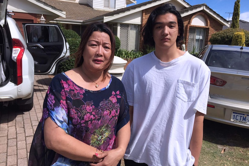 A woman called Cecilia stands alongside her son Daniel standing in the drive of their Canning Vale home with cars behind them.