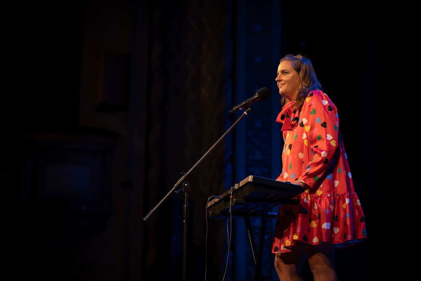 Comedian Sarah Gaul performing on stage with a piano at the Newcastle Civic Theatre.
