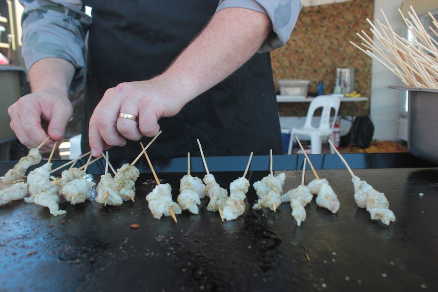 Close up photograph of defence force recruit's hands flipping skewers on bbq.