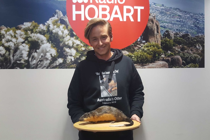 Young man wearing a jumper that says "water rat awareness day" and holding a stuffed rakali