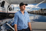 A man poses for a photo in front of a seaplane as it rests in the water