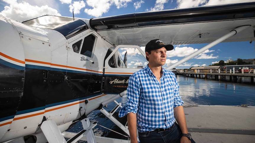 A man poses for a photo in front of a seaplane as it rests in the water