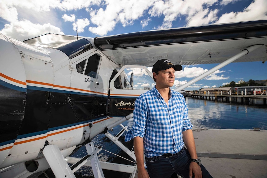 A man poses for a photo in front of a seaplane as it rests in the water