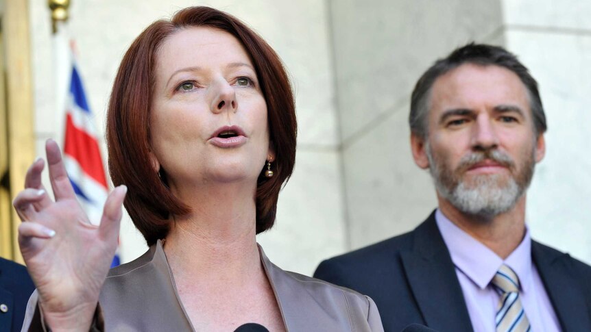 Gillard speaks into a microphone as Rob Oakeshott stands in the background.