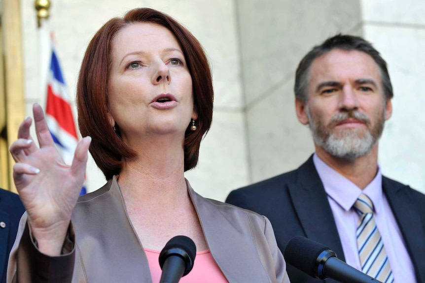 Gillard speaks into a microphone as Rob Oakeshott stands in the background.