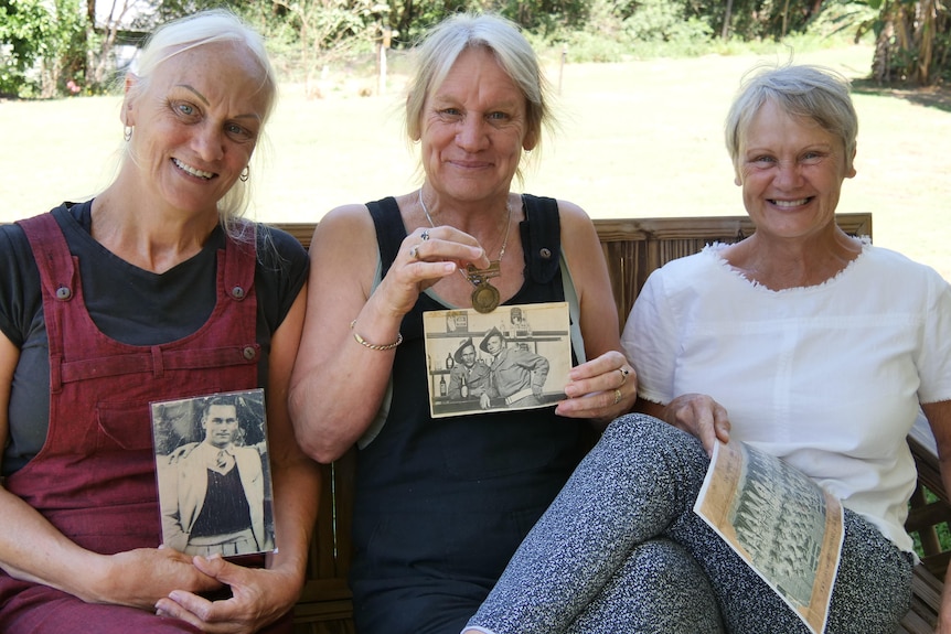 Three women sit on bench holding war photos and a medal