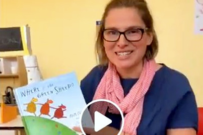 A screen grab of a woman holding a children's book about to read from it.