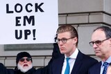 Alex van der Zwaan leaves court. A man standing near the entrance holds a sign that reads 'lock them up!'