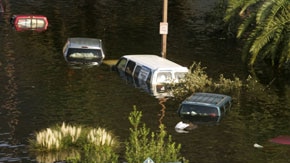 A woman drags a suitcase down the freeway past a flooded Welcome to New Orleans sign