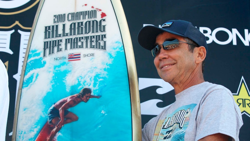 Gerry Lopez holds a retro-design trophy surfboard