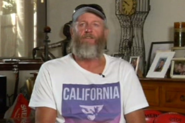 Former AFL player John Barnes, wearing a cap in a t-shirt with beard, looks at the camera