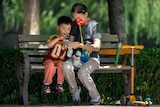 A woman and child are using a mobile phone on a park bench. 