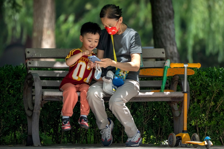 A woman and child are using a mobile phone on a park bench. 