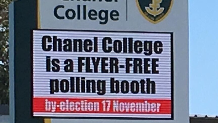 A school sign displays 'Chanel College is a flyer-free polling booth', with trees and blue sky in background