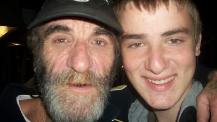 man with a grey beard and black cap with younger man, both smiling