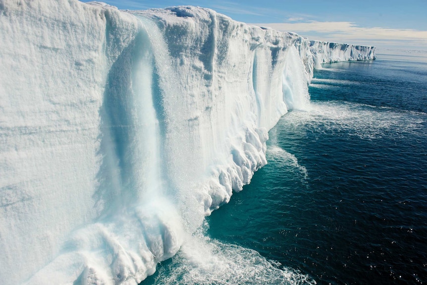 Waterfalls running off an ice wall into the ocean.