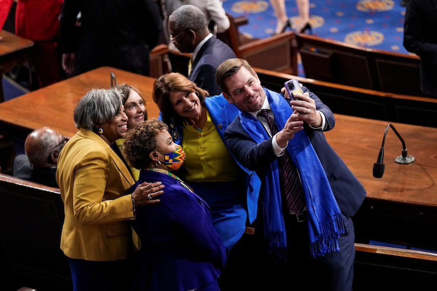 A group of people in blue and yellow huddle together while taking a selfie