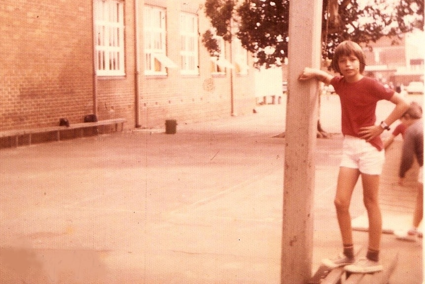A boy leans against a telephone pole.