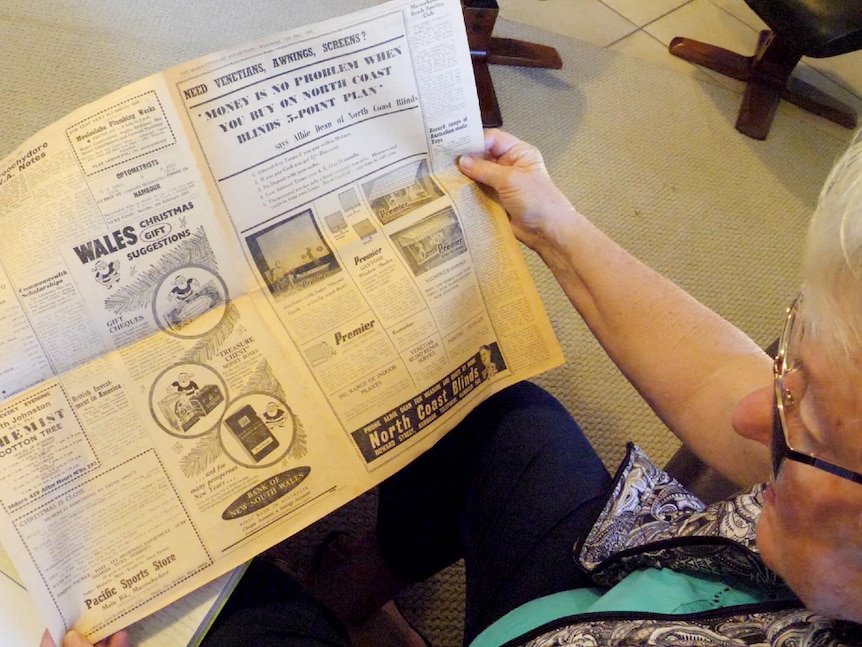 Peering over the shoulder of an older woman who is reading a newspaper from 1962.