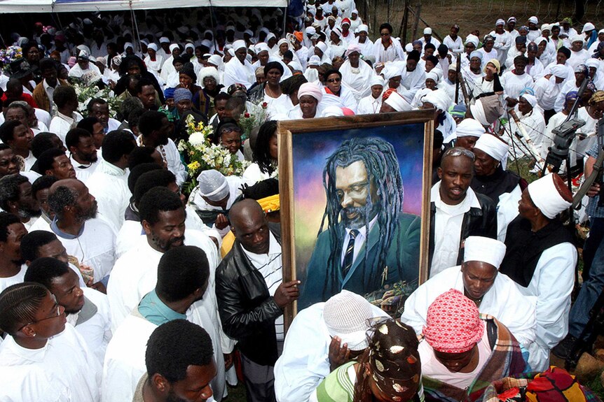 Large crowd of mourners dressed in white carrying a poster of Lucky Dube.