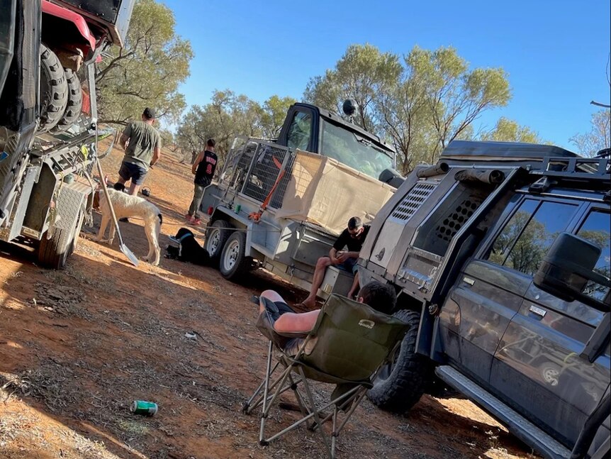 Several men, cars and chairs at a camping set up in outback Queensland.