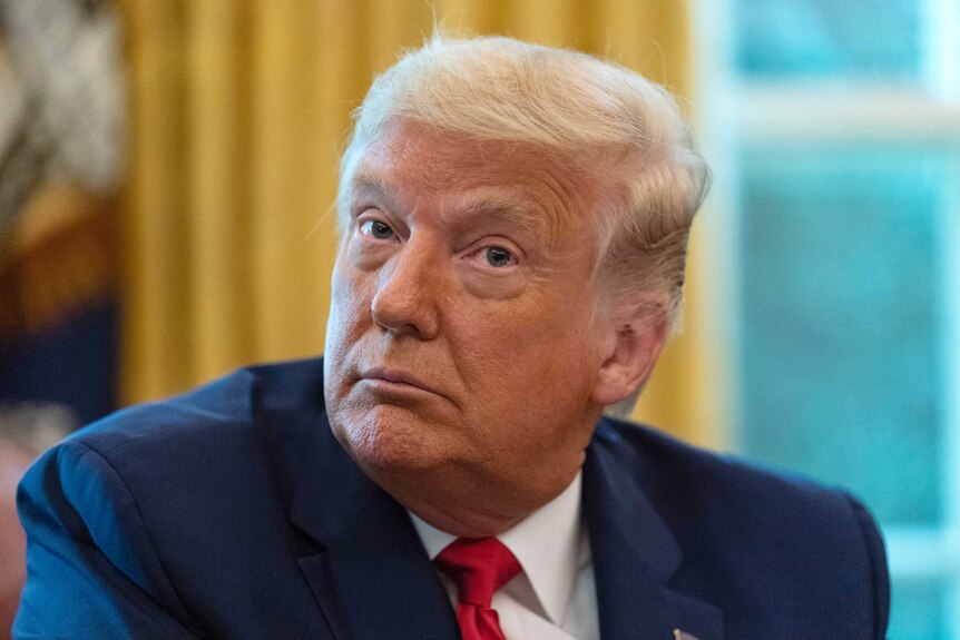 President Donald Trump turns his head to the side while listening.