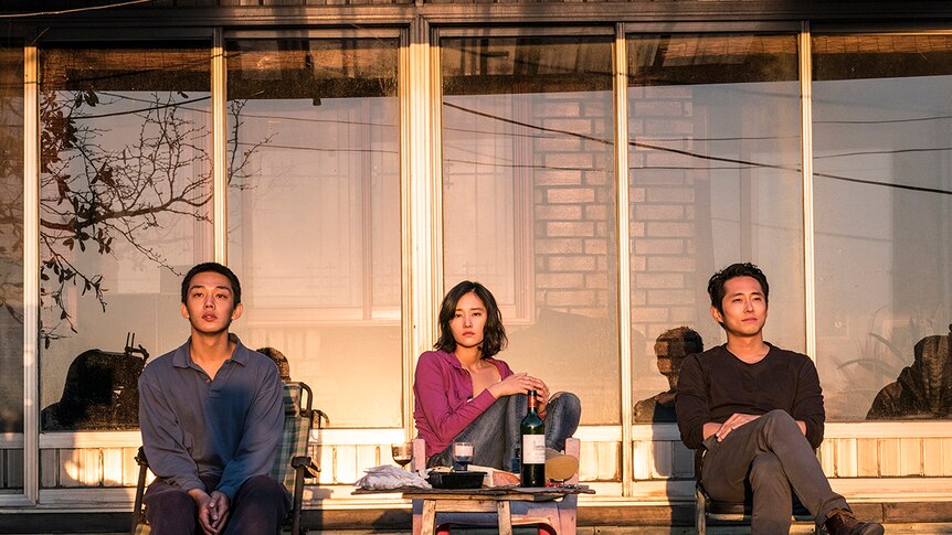 Colour still of Yoo Ah-in, Jeon Jong-seo and Steven Yeun sitting and watching sunset in 2018 film Burning.