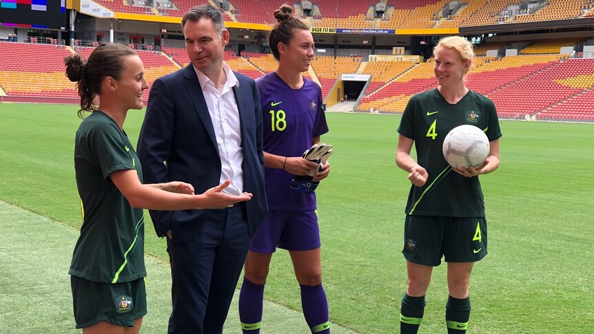Ante Milicic stands next to the Lsng Park playing surface speaking to three Matildas players.