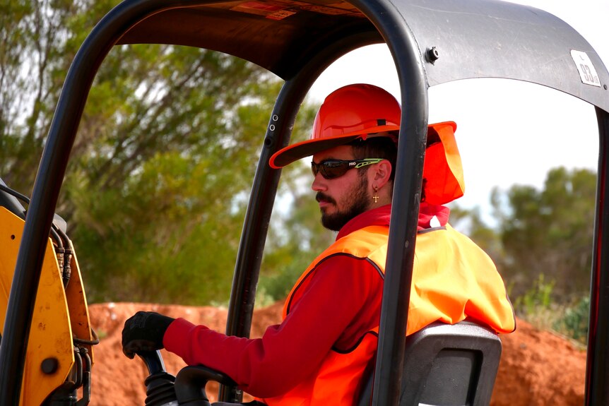 A young man in high-vis operates an excavator.