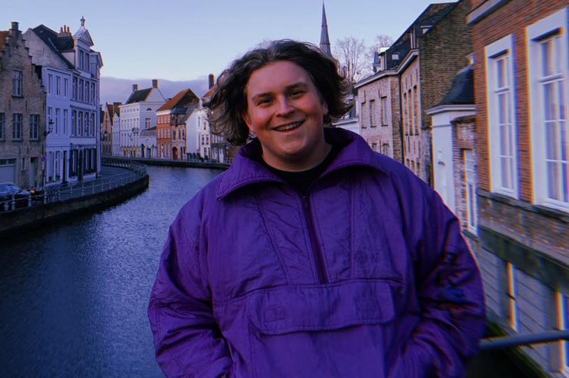 A young man stands in front of a canal and homes.