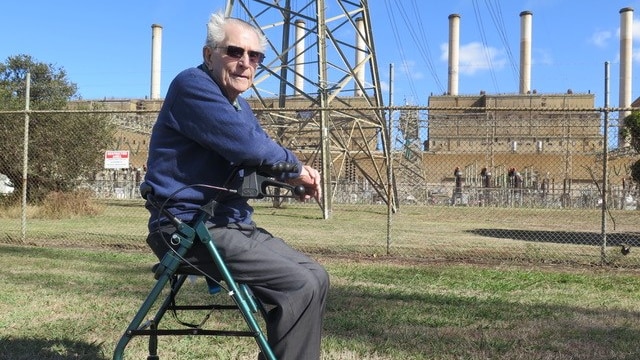 Reg sits on his walker's seat in front of the high fences containing the Hazelwood plant