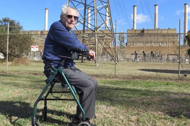 Reg sits on his walker's seat in front of the high fences containing the Hazelwood plant