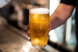 A close-up shot of a hand holding a full pint of beer below a beer tap after pouring it at a bar in a pub.