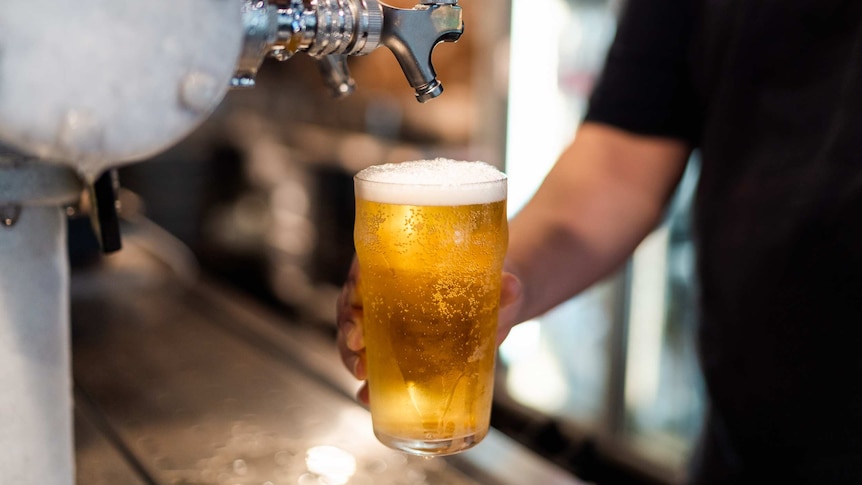 A close-up shot of a hand holding a full pint of beer below a beer tap after pouring it at a bar in a pub.