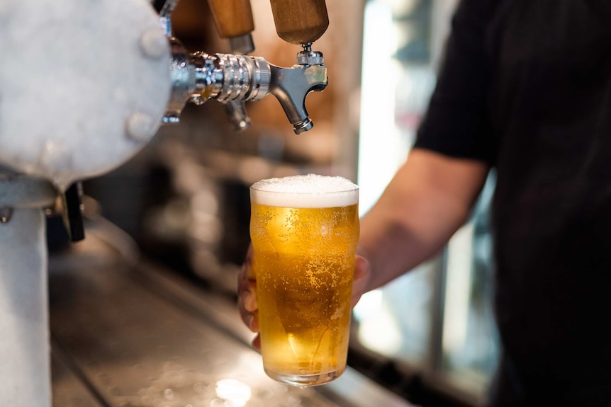 A close-up shot of a hand holding a full pint of beer below a beer tap after pouring it at a bar in a pub.