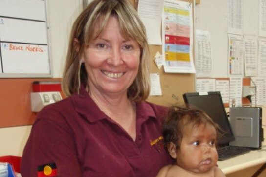 A woman in a maroon shirt smiles while holding a baby
