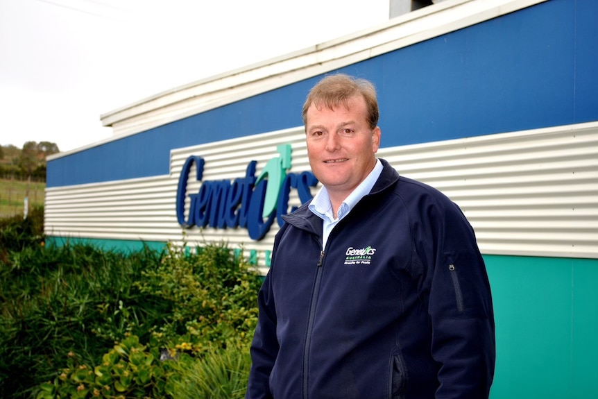 A man in a blue sweater stands in front of a sign