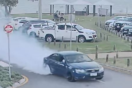 A blue Ford Falcon doing a burnout with smoke coming from rear tyres.