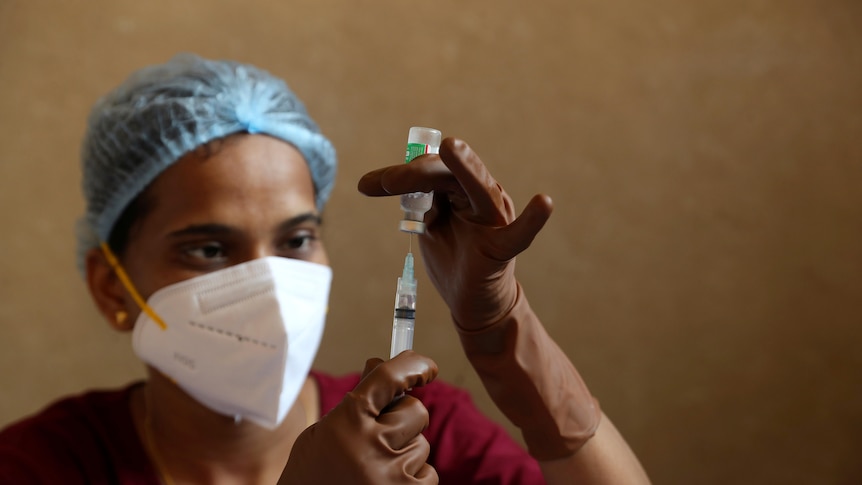 A health worker fills a syringe with a vial of COVID vaccine
