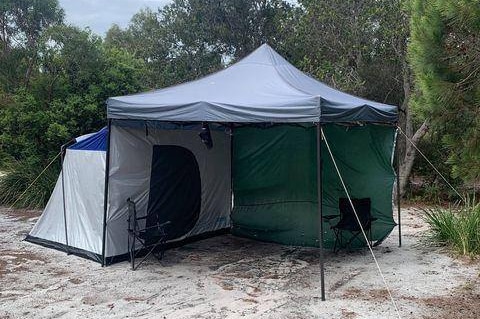 An unoccupied tent with two camp chairs underneath an awning.