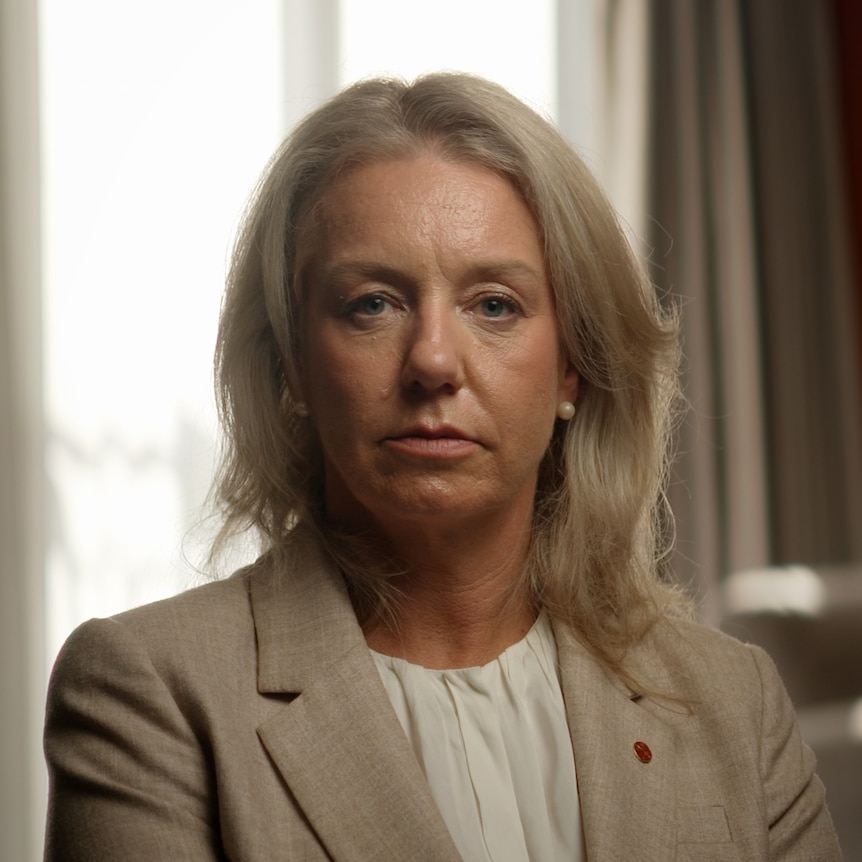 Bridget McKenzie sits in a room wearing a fawn blazer, looking into camera with a serious expression.